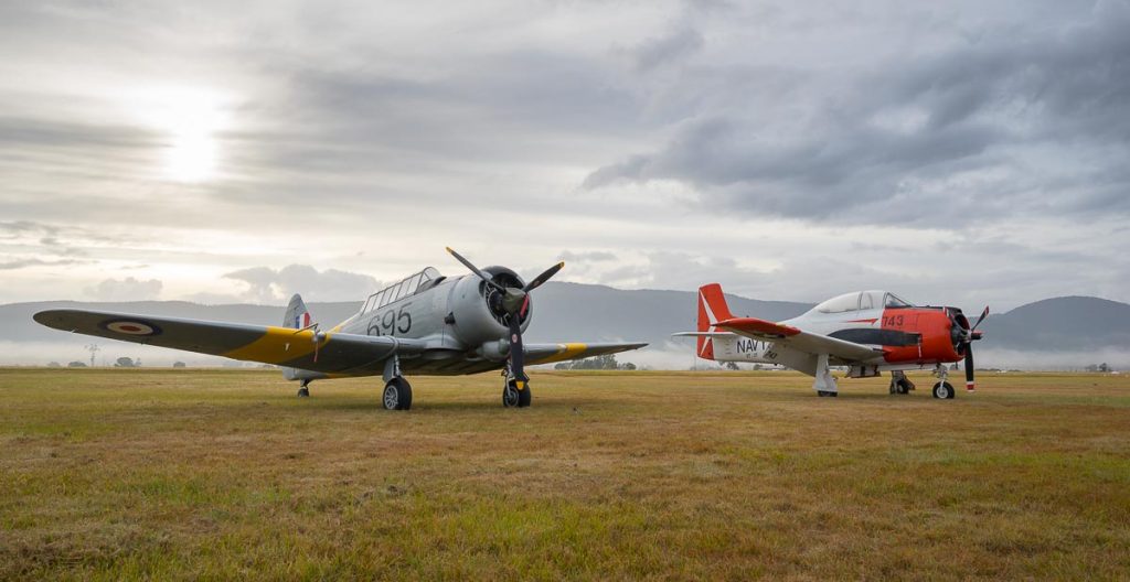 CAC CA-16 Wirraway VH-MFW and North American T-28B Trojan VH-RPX "Miss Stress" on the flight line in a foggy sunrise.