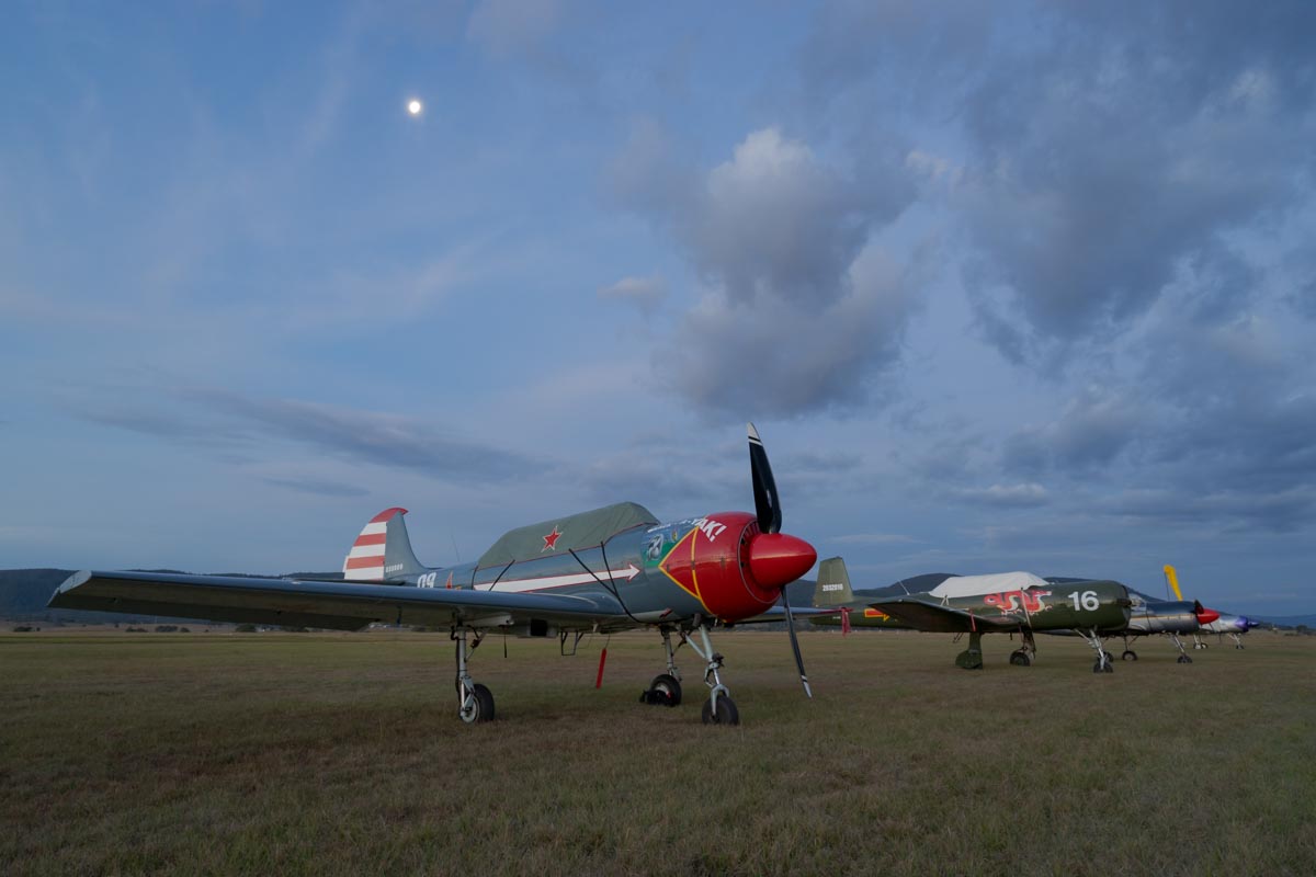 The moon rises over Yakovlev Yak-52 trainer VH-YYC "Crack-A-Yak" and other aircraft at dusk.